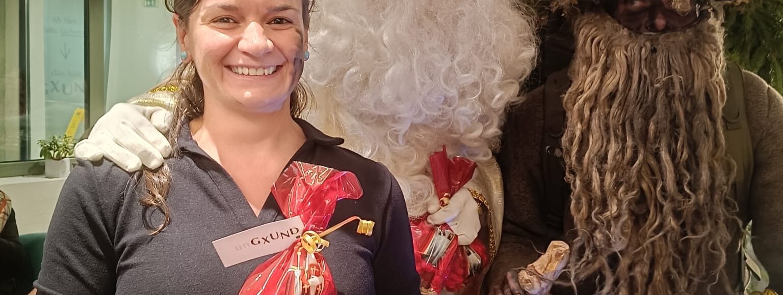 Ungxund Krampuskraenzchen Nikolaus Körbler übergeben Servicemitarbeiterin ein rots Nikolaussackerl