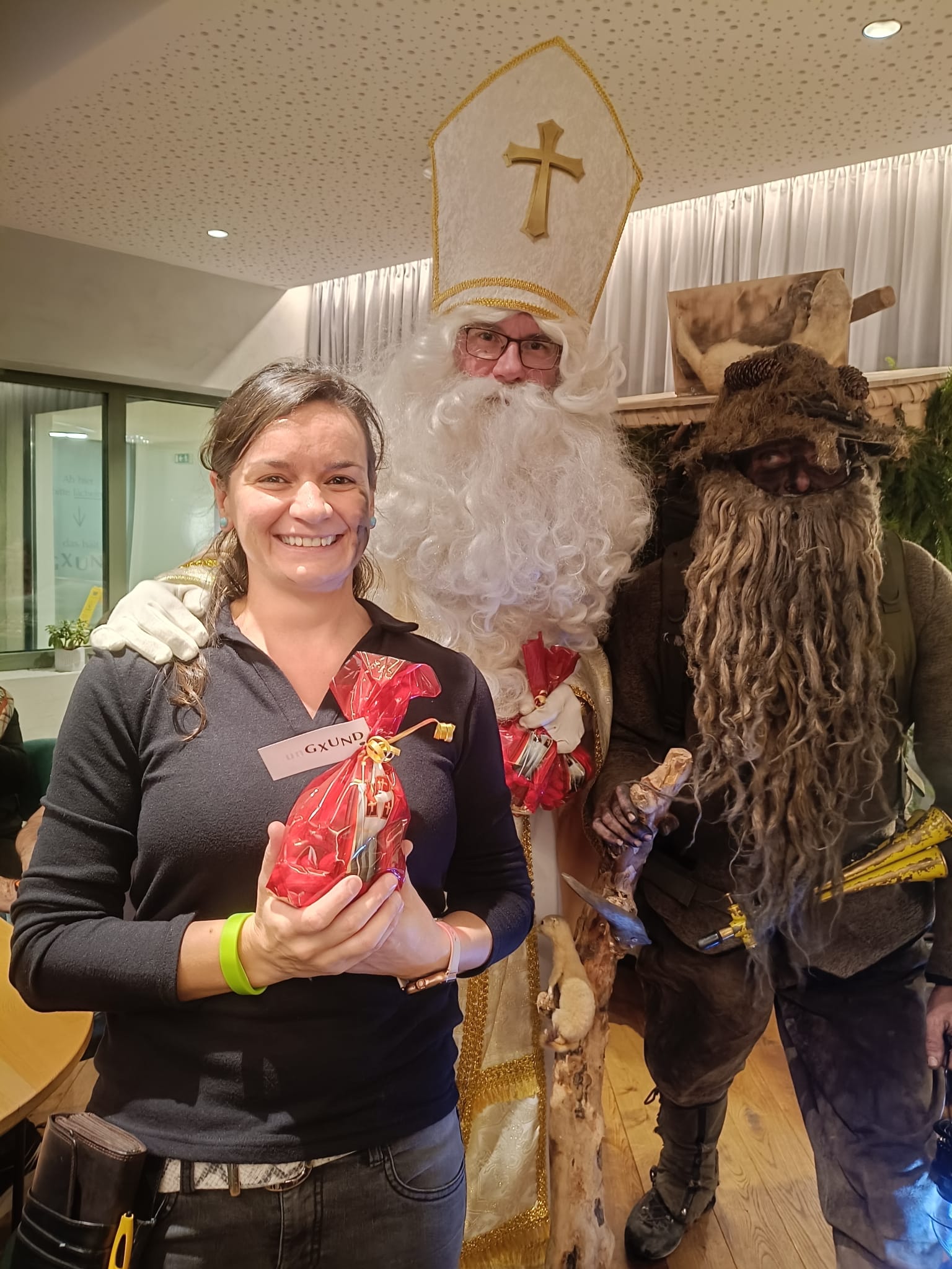 Ungxund Krampuskraenzchen Nikolaus Körbler übergeben Servicemitarbeiterin ein rots Nikolaussackerl